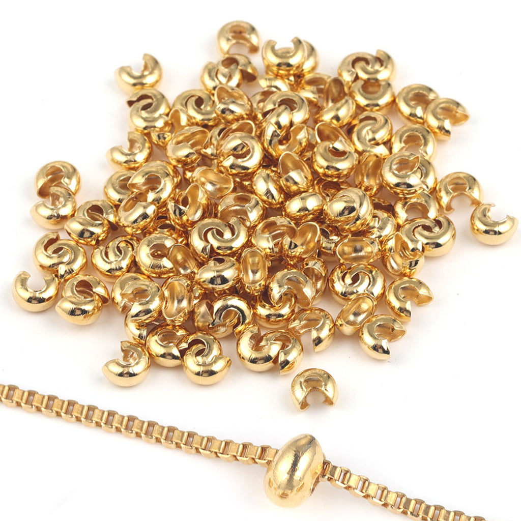 Pile of small gold C-shaped crimp bead covers with a gold chain and oval bead on white background.