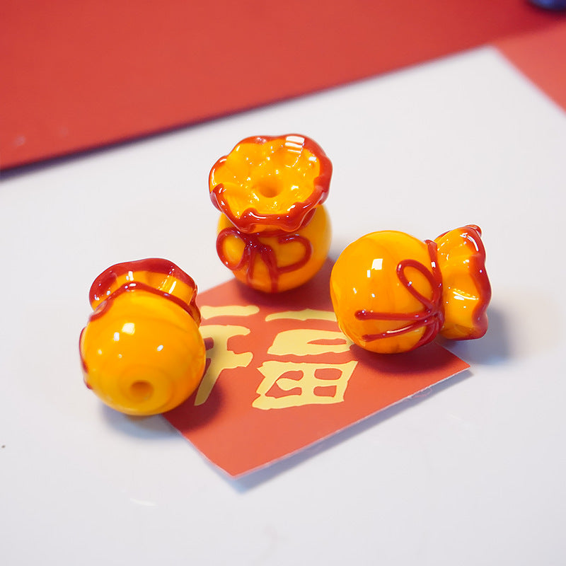 Three glossy orange and red decorative figurines shaped like small money bags or pouches, arranged on a white surface with a red card featuring gold characters.