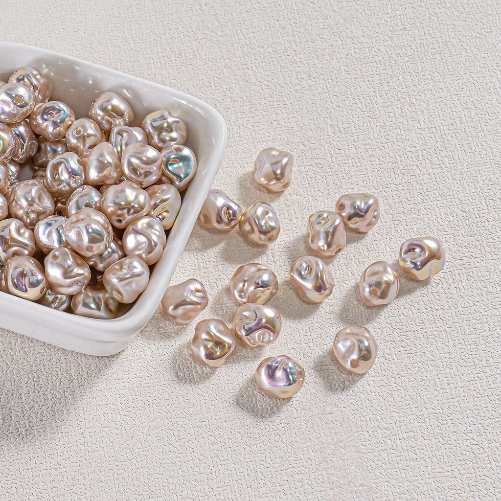 Iridescent champagne-gold baroque faux pearl beads in a white ceramic bowl with several scattered on a beige surface