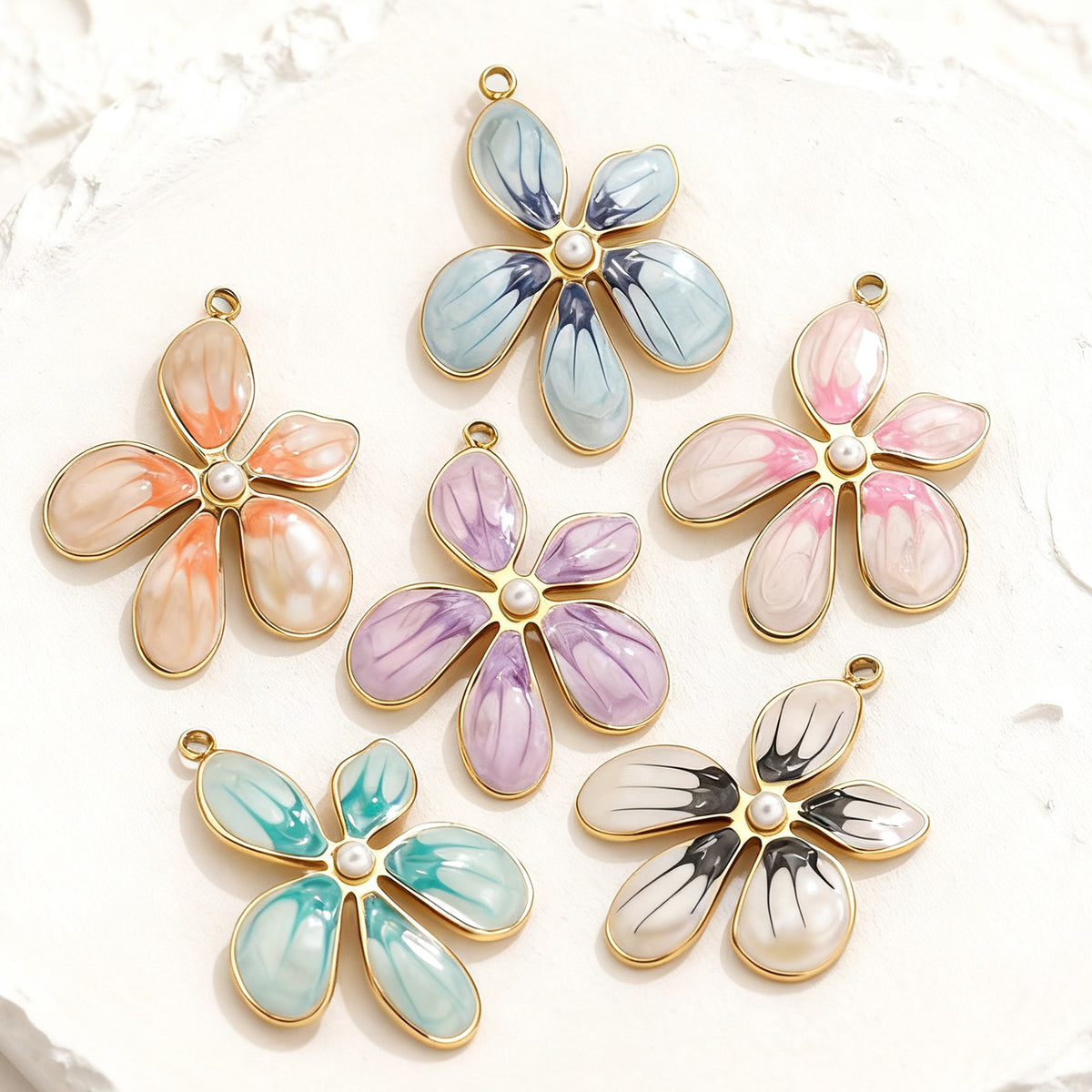 Six gold-toned enamel flower pendant charms with pearl centers in blue, orange, pink, purple, teal, and black and white