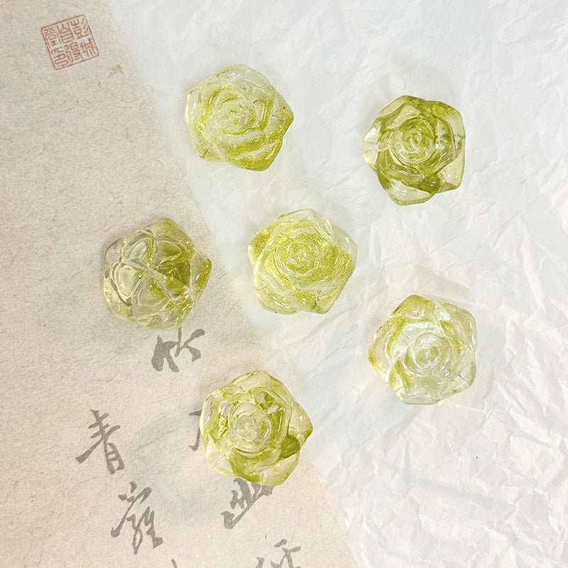 Five translucent pale yellow rose-shaped glass beads on a textured white surface with beige calligraphy paper