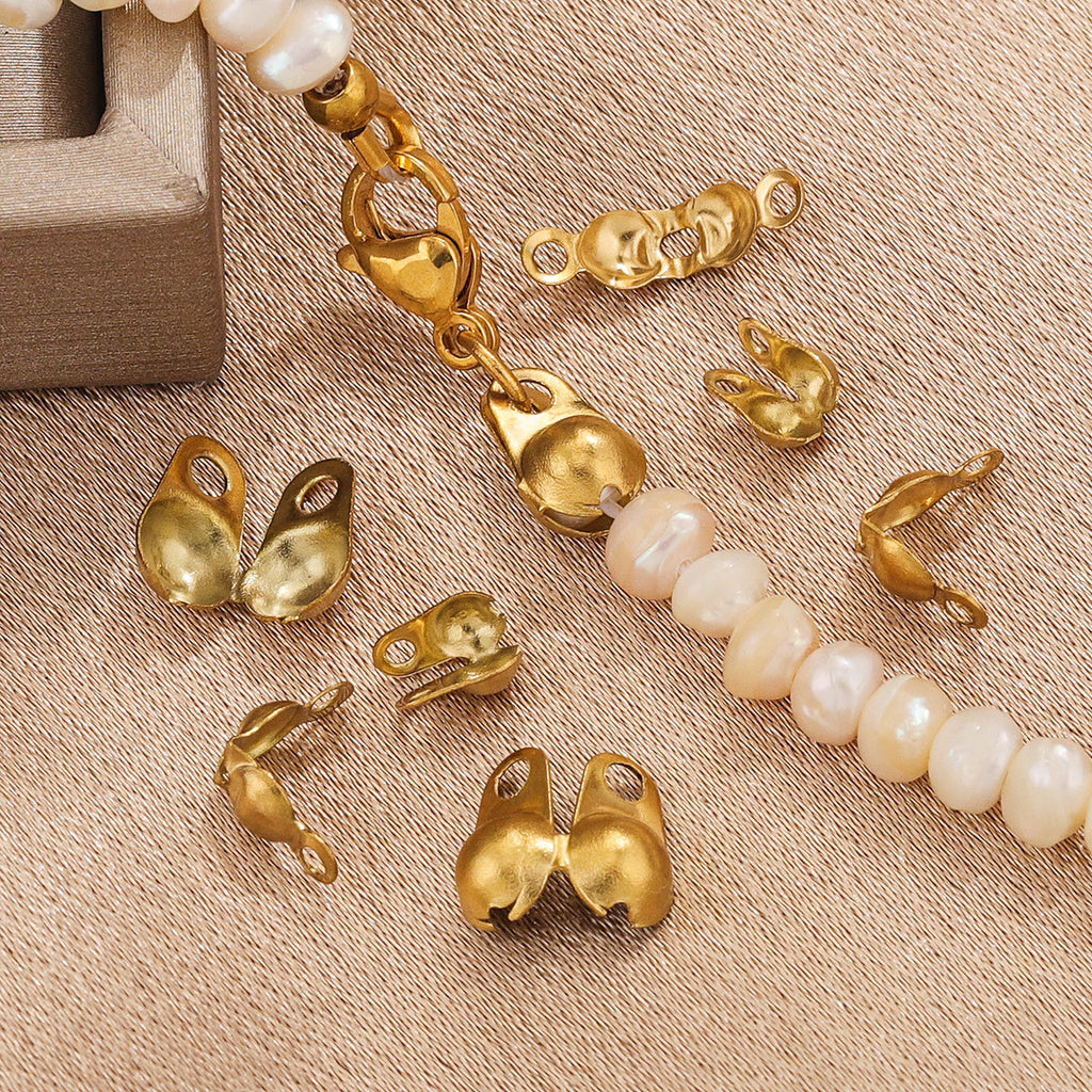 Gold ball chain connector clasps scattered on beige fabric with a partial strand of white baroque beads