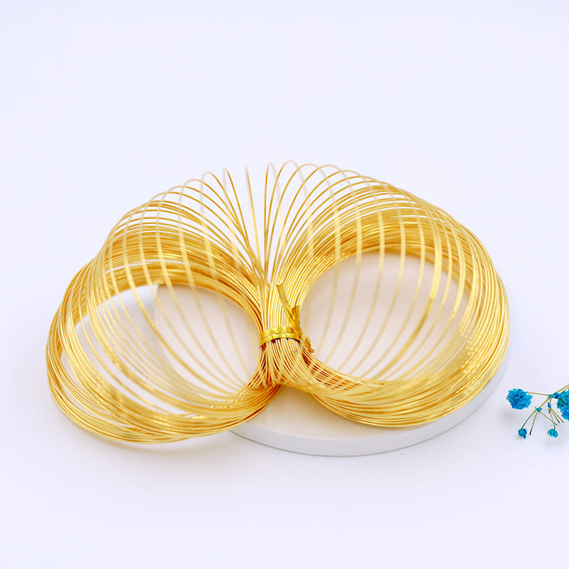 Gold-plated spiral memory wire bangle bracelets tied together on white circular stand with blue flower