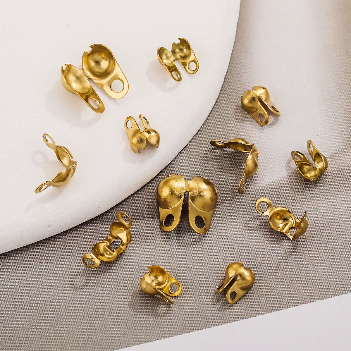 Multiple small gold-toned ball chain connector clasps arranged on a light surface with a white curved prop