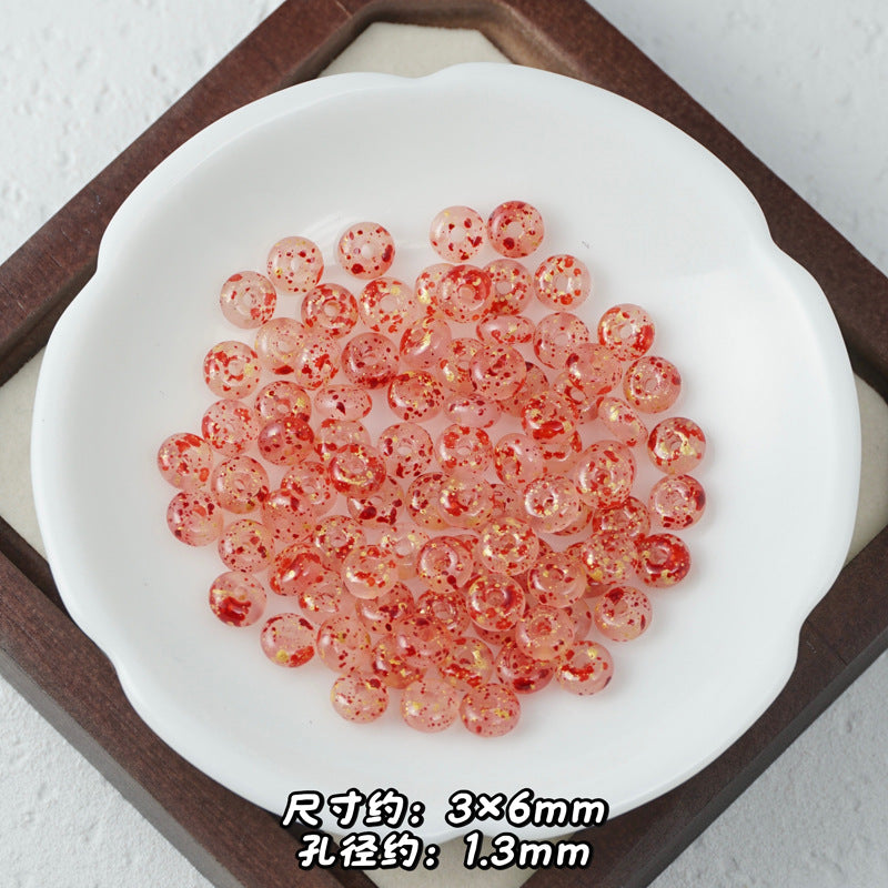 Translucent pink Picasso glass abacus beads with red glitter speckles piled on a white scalloped dish.