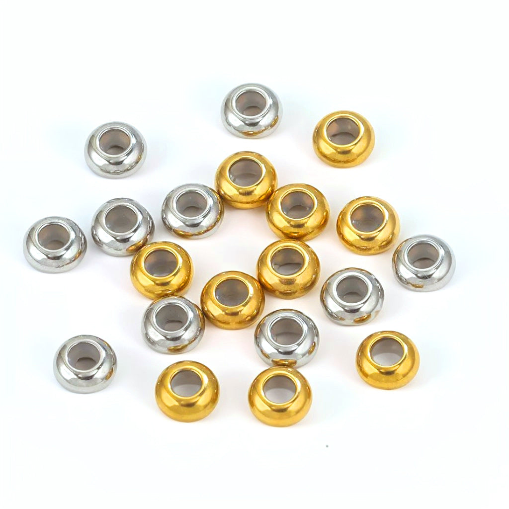 Gold and silver stainless steel flat abacus stopper beads scattered on white, showing center holes