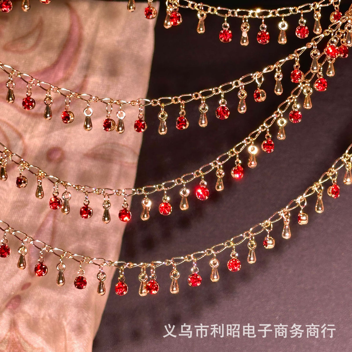Gold chains with dangling red teardrop rhinestones draped over pink and dark fabric