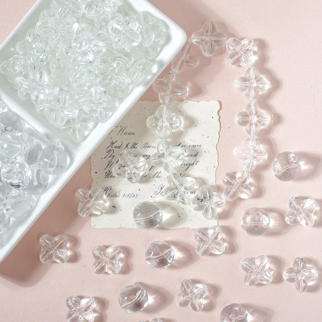 Clear flower-shaped glass beads on a pink background with a white tray and a vintage-style note