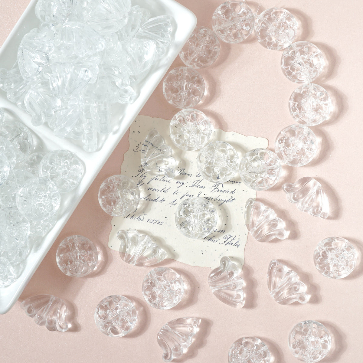 Clear engraved glass beads and charms on pale pink with a white tray and handwritten note