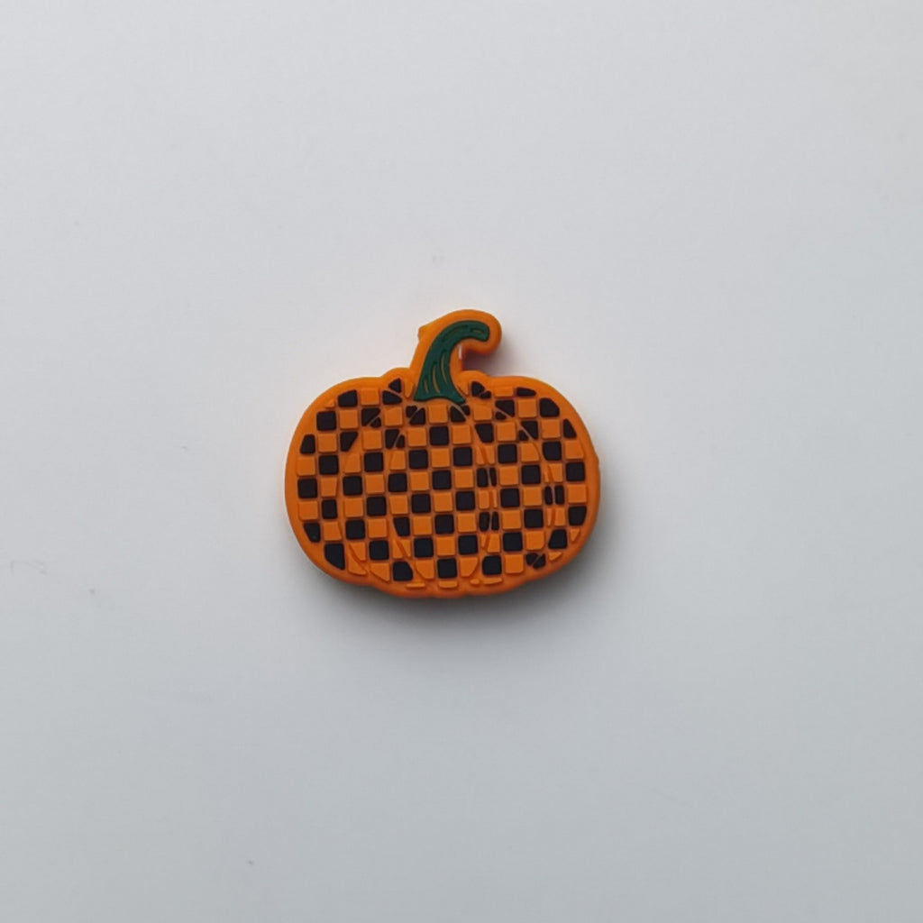 An orange pumpkin-shaped accessory with a black checkered pattern and a green stem, photographed on a plain light gray background.