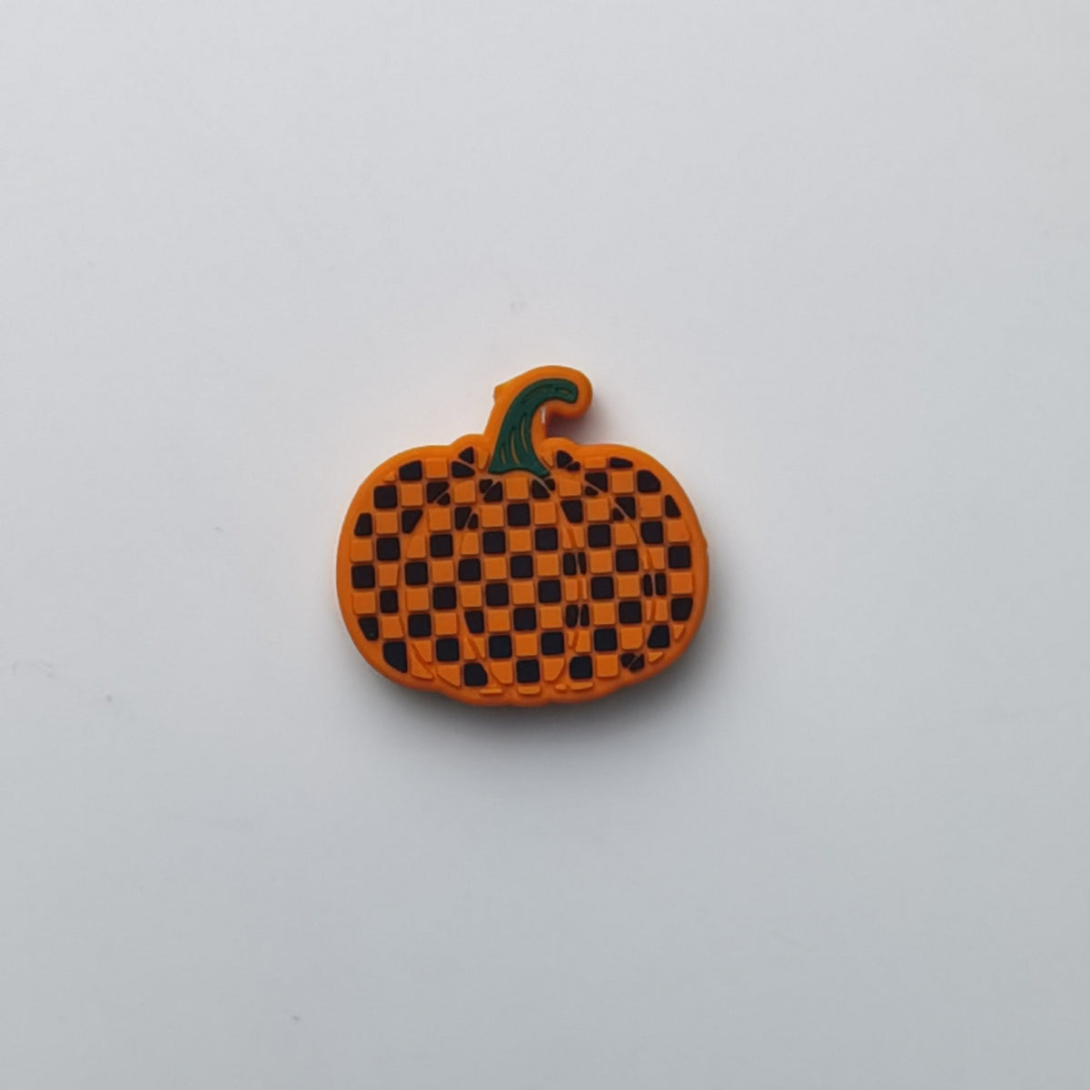 An orange pumpkin-shaped accessory with a black checkered pattern and a green stem, photographed on a plain light gray background.