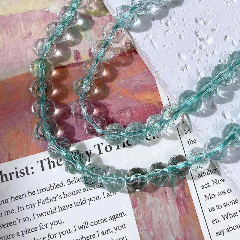 Beaded necklace of faceted clear aqua-blue glass beads on translucent thread over printed paper and textured white paper
