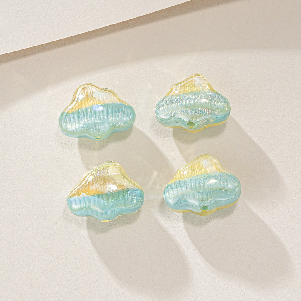 Four small cloud-shaped translucent beads in light blue and pale yellow, arranged on a warm off-white surface.