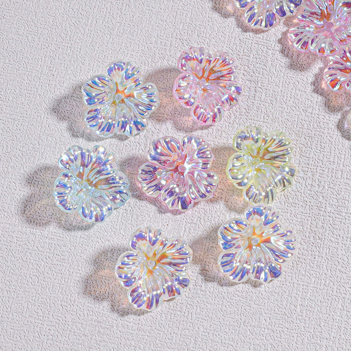 Iridescent resin flower beads in pastel pink, blue, purple and yellow on a textured white surface