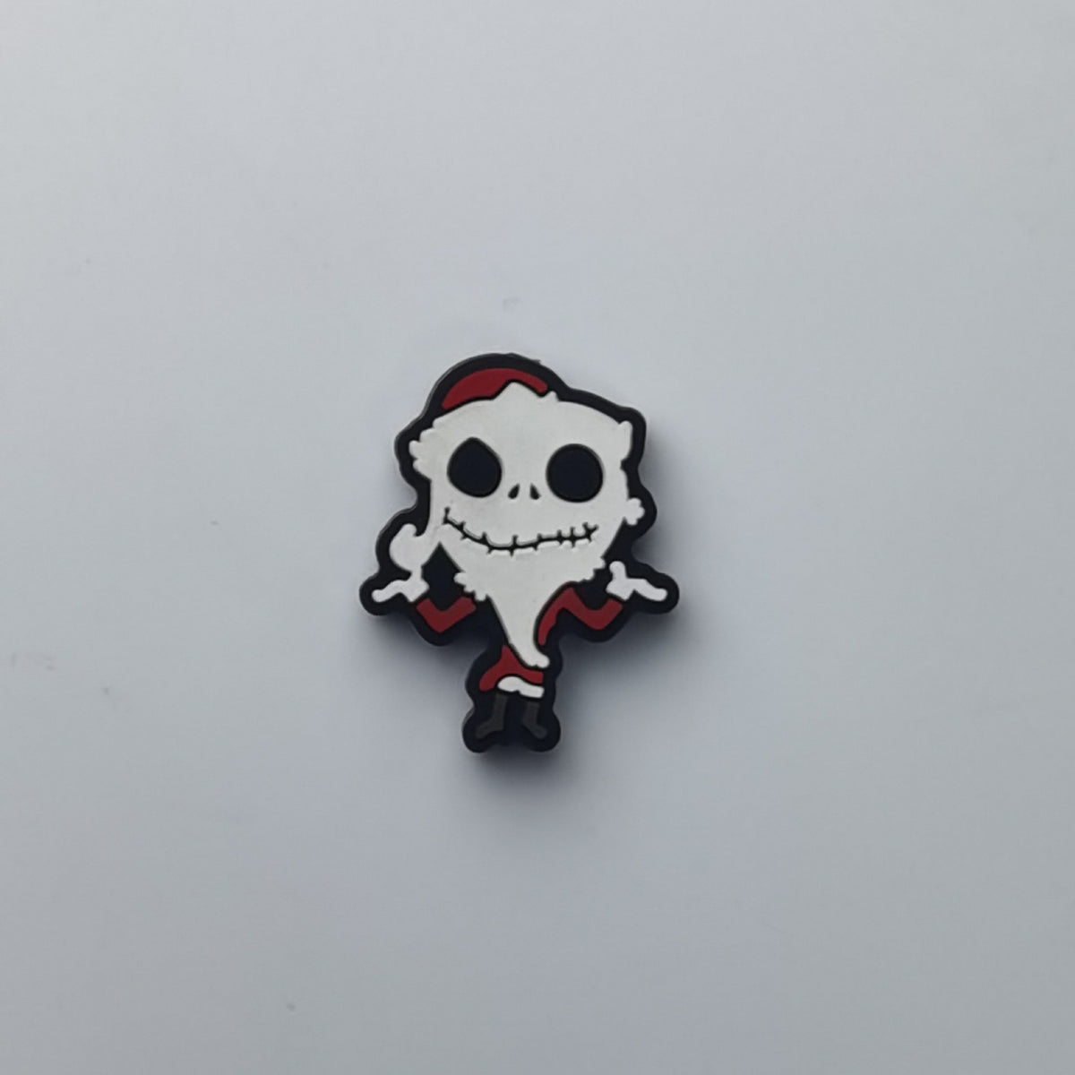 A small cartoon skull character charm or pin wearing a red Santa hat and red clothing, shown on a plain light gray background.