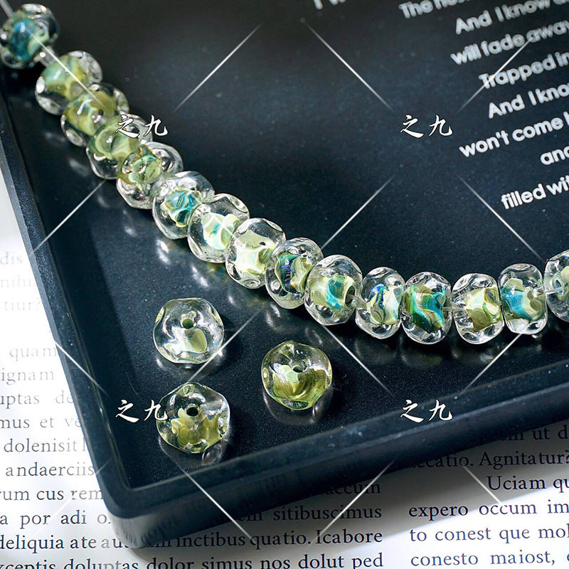 Faceted clear lampwork beads with marbled green-yellow-blue pattern on a black tray, loose beads