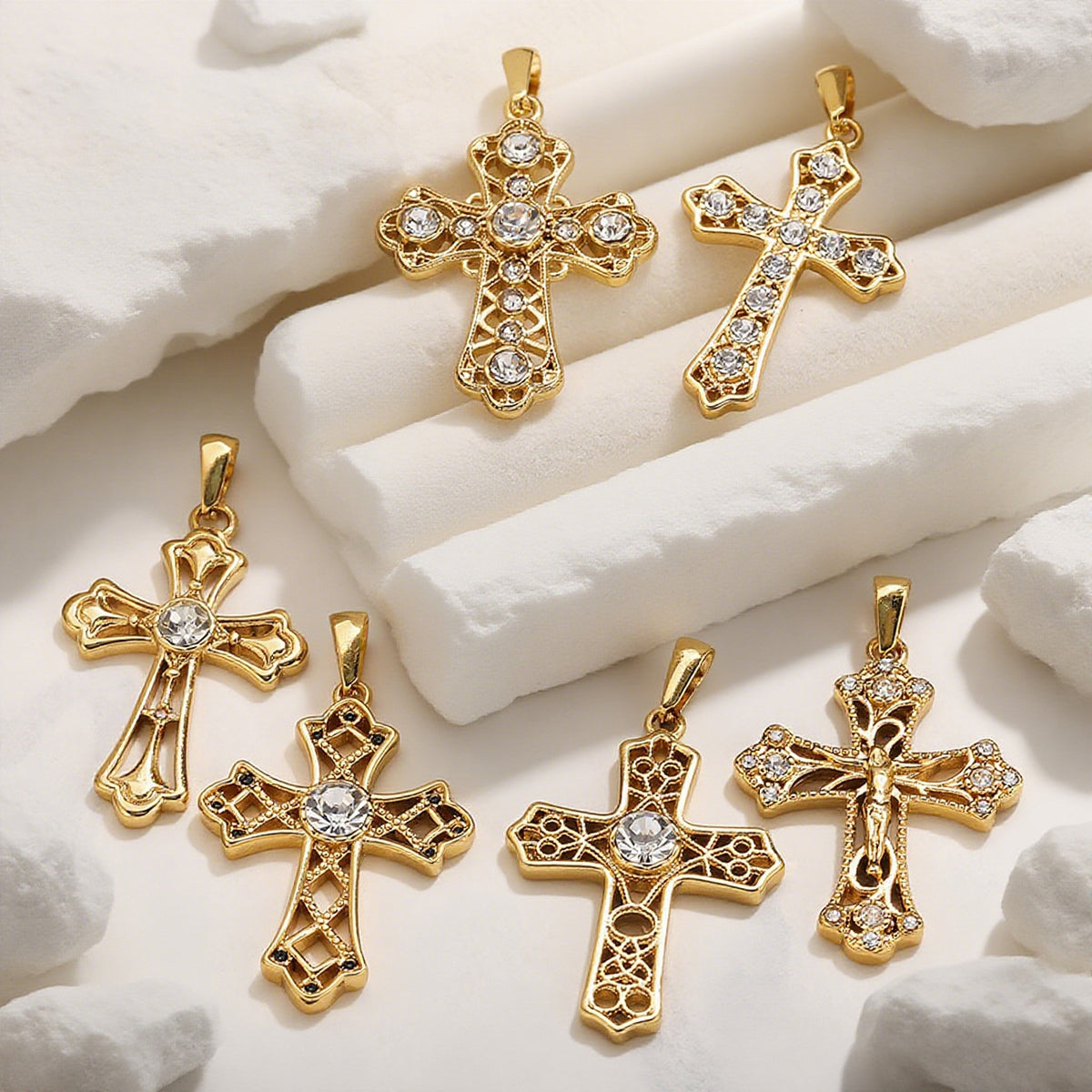 Six gold cross pendants with clear rhinestone accents arranged on white textured foam blocks