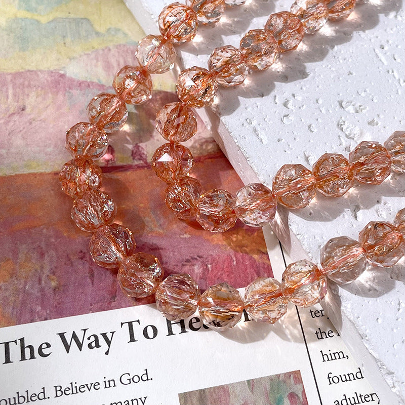Strand of faceted clear beads with copper inclusions draped across a textured white surface and colorful printed paper