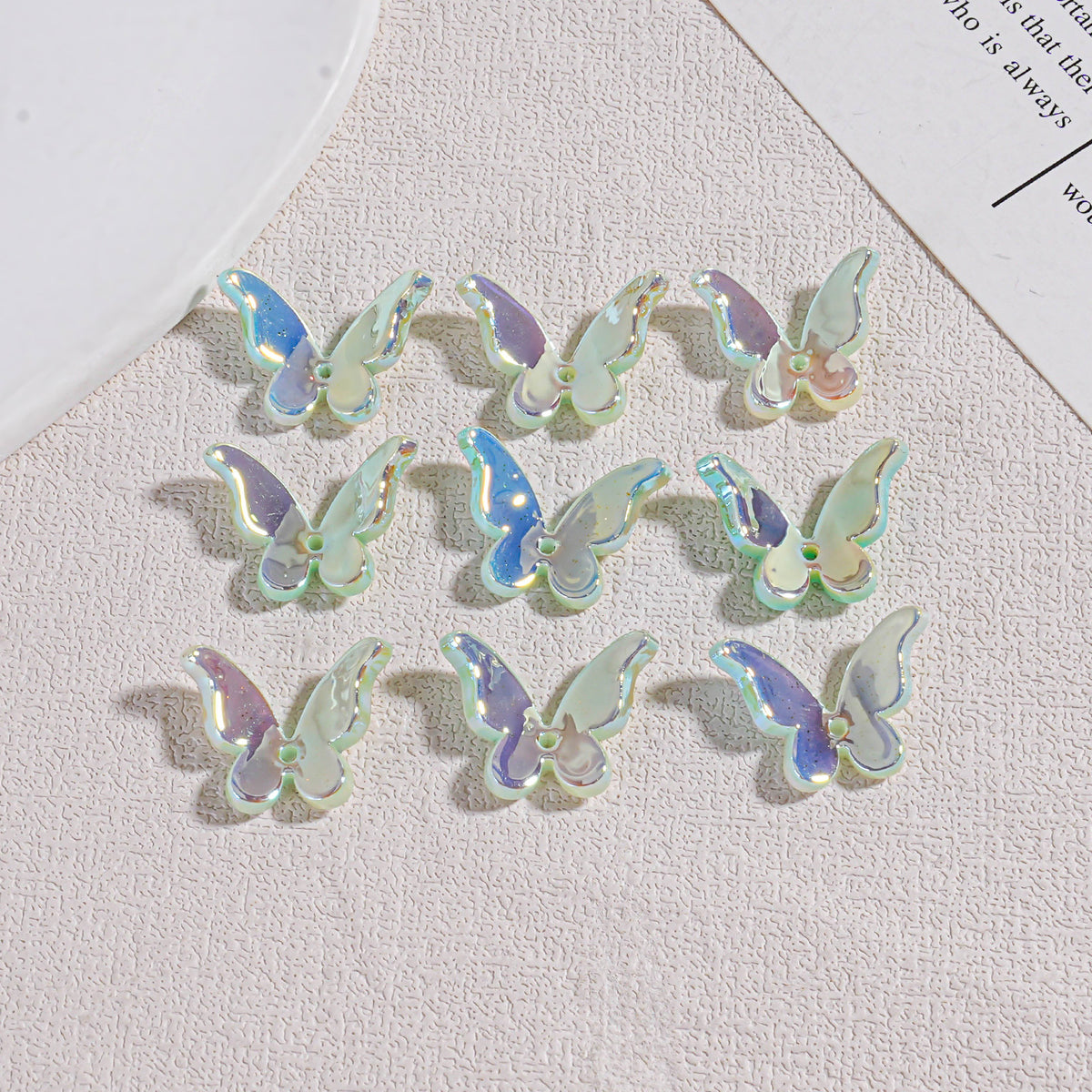 Nine iridescent butterfly acrylic beads in 3x3 grid on beige surface with plate and paper edges