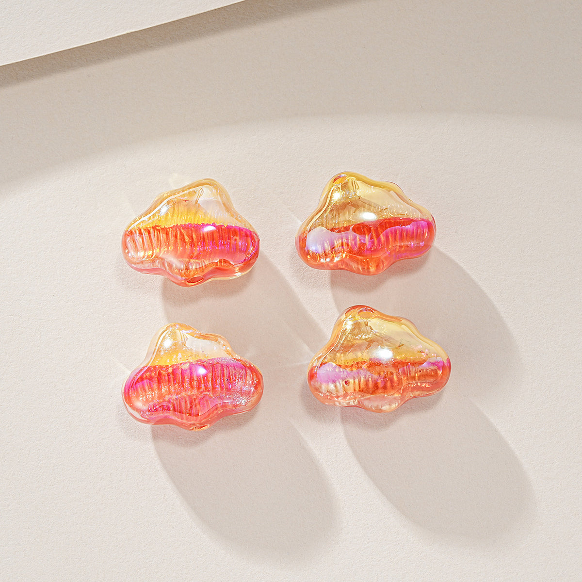 Four cloud-shaped translucent resin beads with pink and orange gradient in a 2x2 grid on light beige.