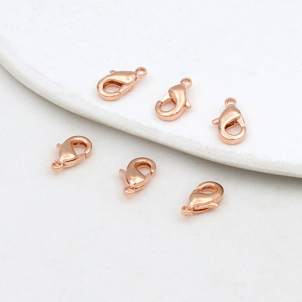 Six rose gold teardrop lobster clasps on a white marble surface