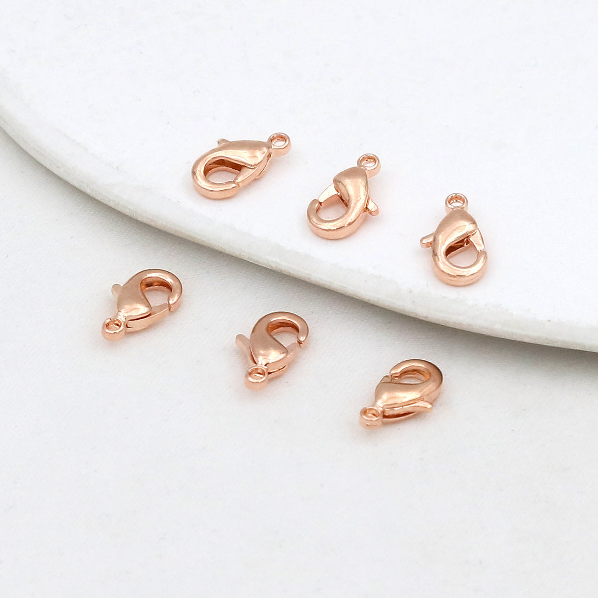 Six rose gold teardrop lobster clasps on a white marble surface