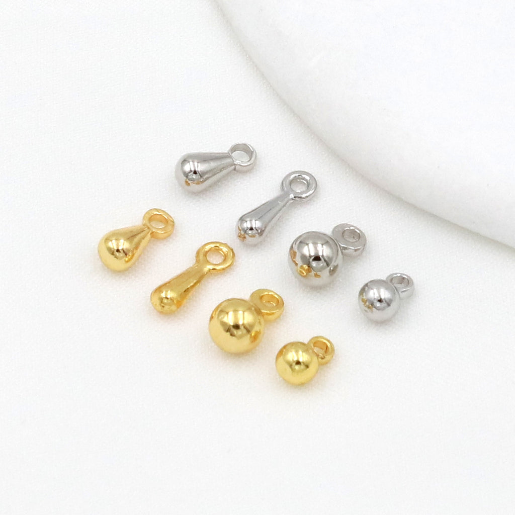 Gold-plated ball and teardrop chain-end charms in gold and silver tones arranged on a white surface