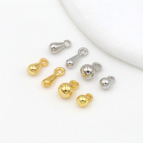 Gold-plated ball and teardrop chain-end charms in gold and silver tones arranged on a white surface