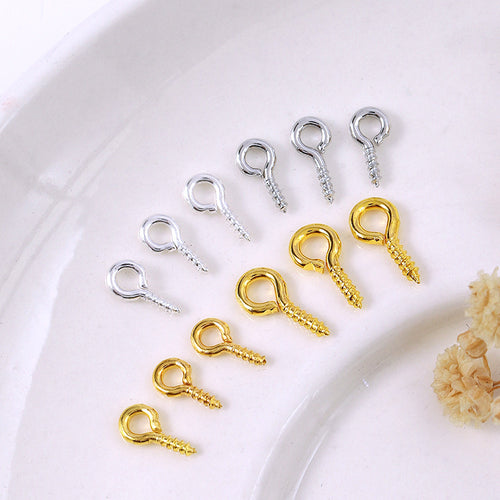 Small screw eye pins in silver and gold finishes arranged diagonally on white ceramic