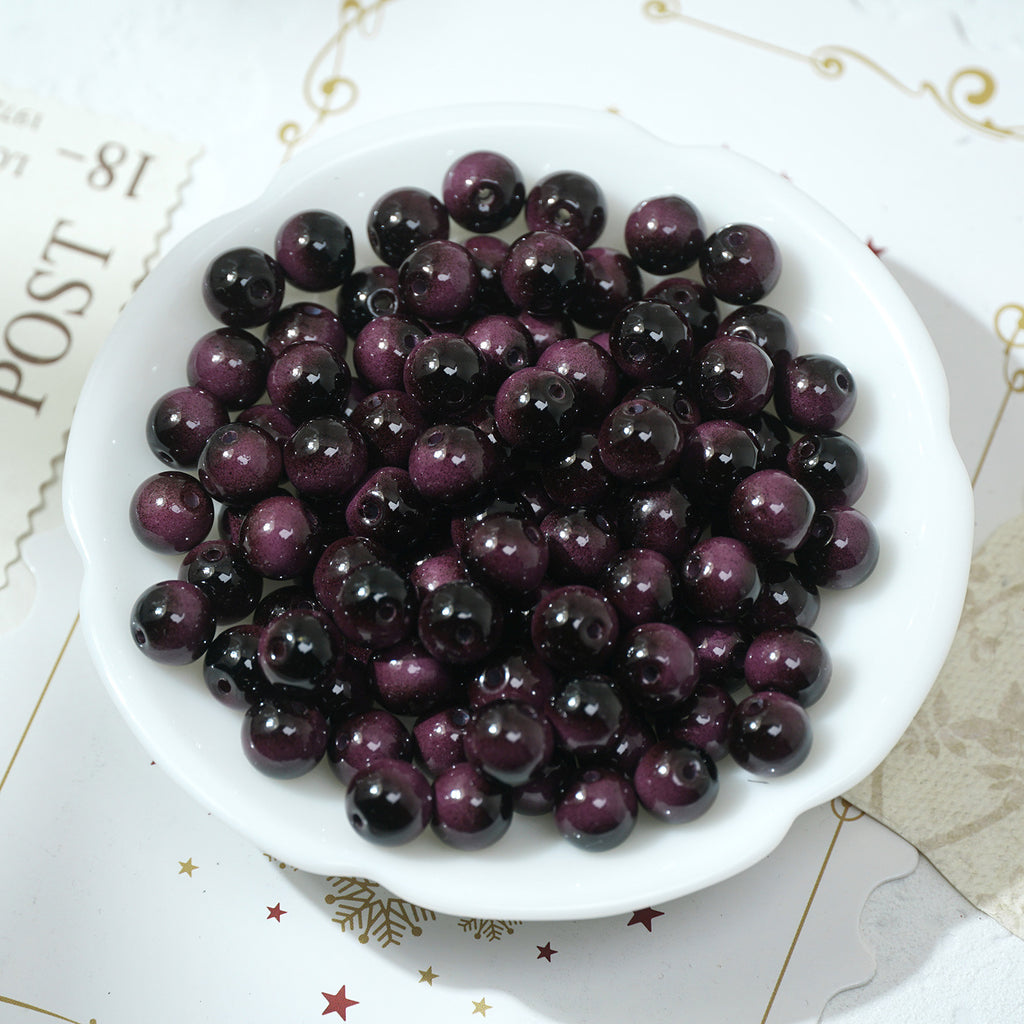 Round glossy dark purple and black tiger's eye glass beads in a white bowl