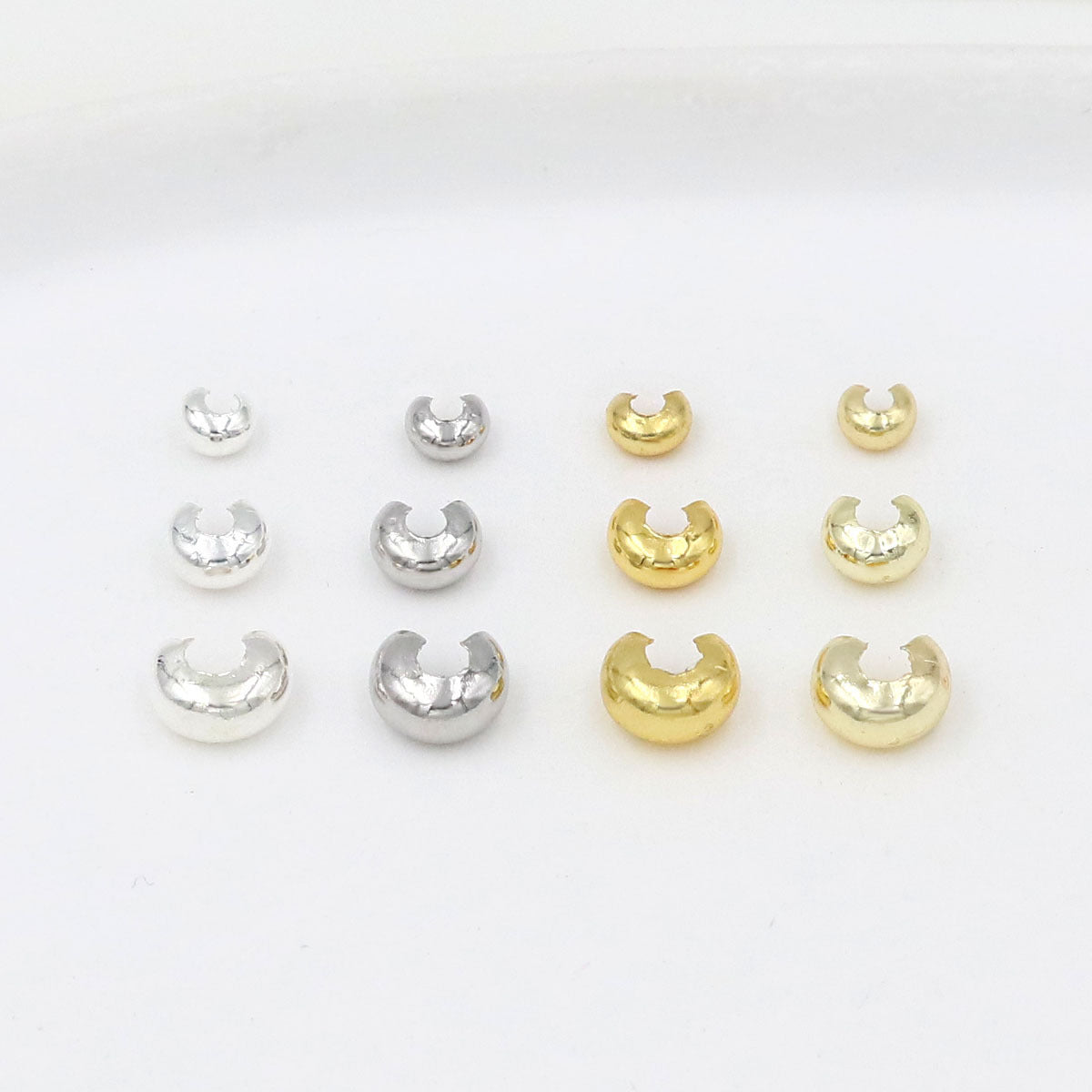 Twelve C-shaped crimp bead covers in three sizes and silver and gold finishes arranged in three rows on white