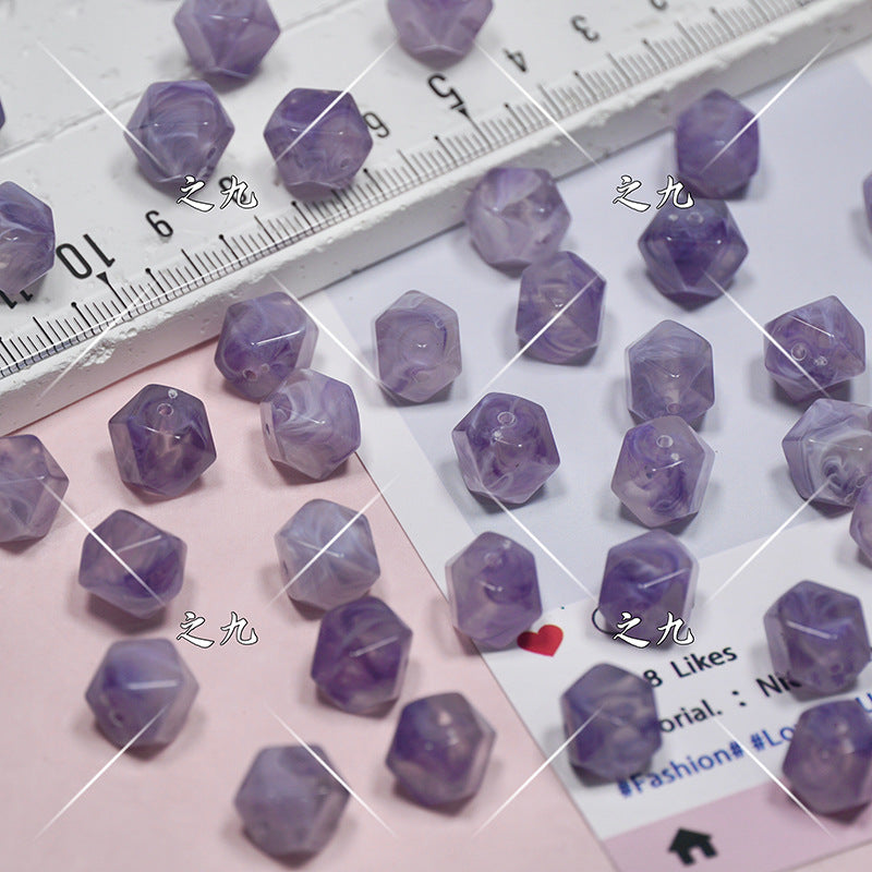 Small faceted purple beads scattered on a pink and white surface with a ruler