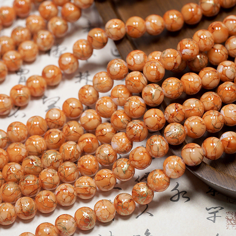 Close-up of orange-brown marbled porcelain beads with gold veining on a light surface
