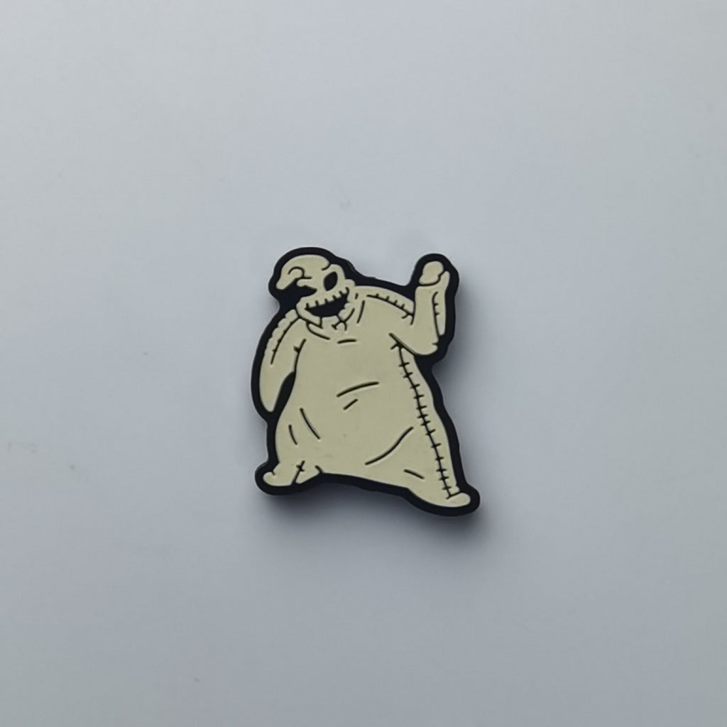 A small cartoon ghost-shaped accessory with a pale beige body, black outline, and stitched details, photographed on a plain light gray background.