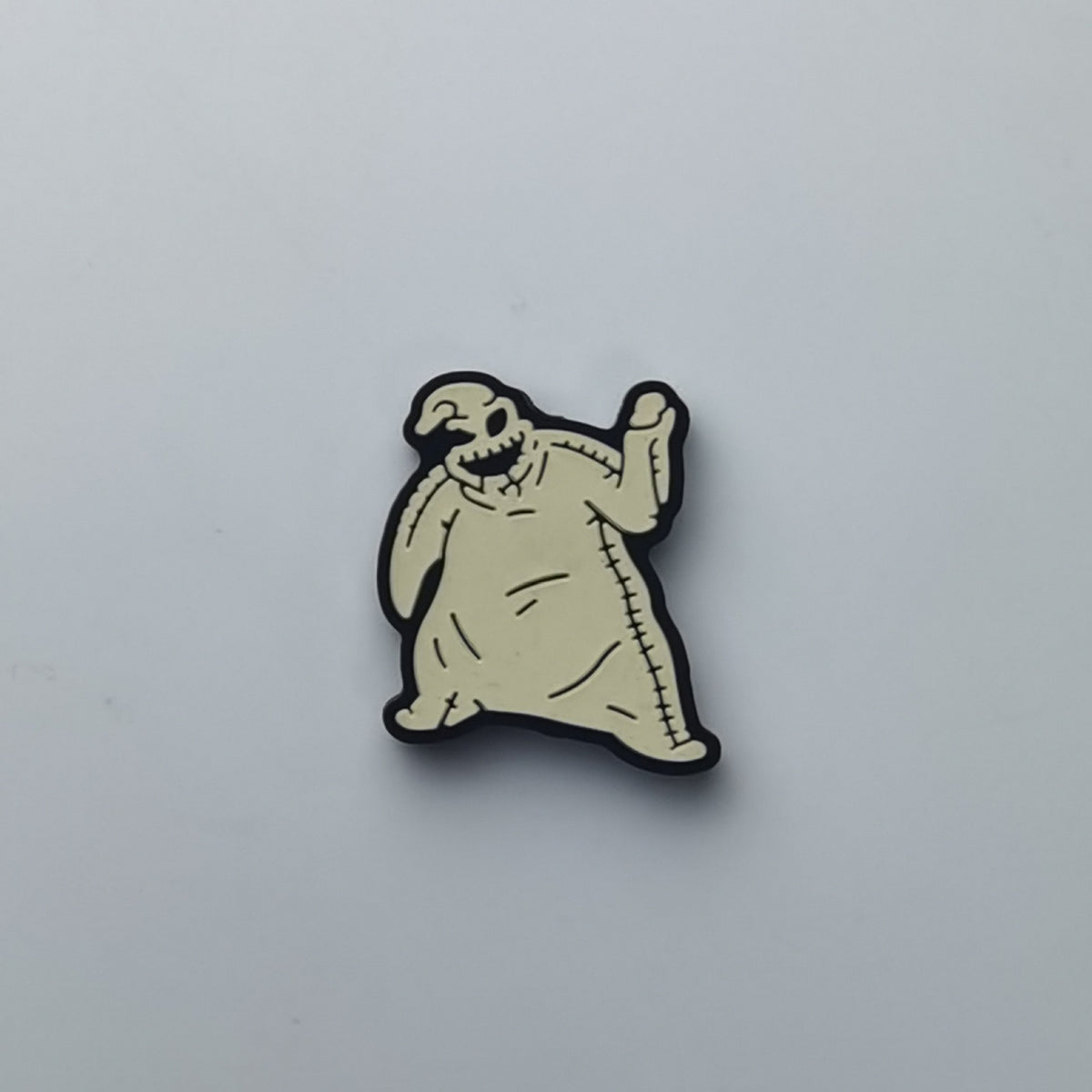A small cartoon ghost-shaped accessory with a pale beige body, black outline, and stitched details, photographed on a plain light gray background.