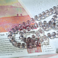 A close-up of a strand of faceted clear beads with a subtle lavender tint, draped over printed paper.