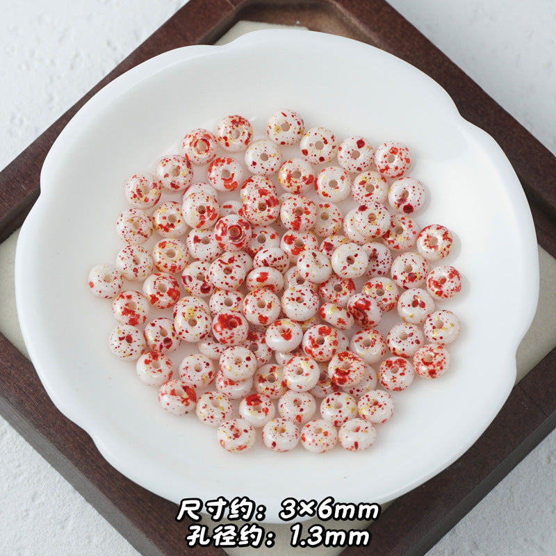 White Picasso glass abacus beads with red speckled pattern in a white ceramic dish.