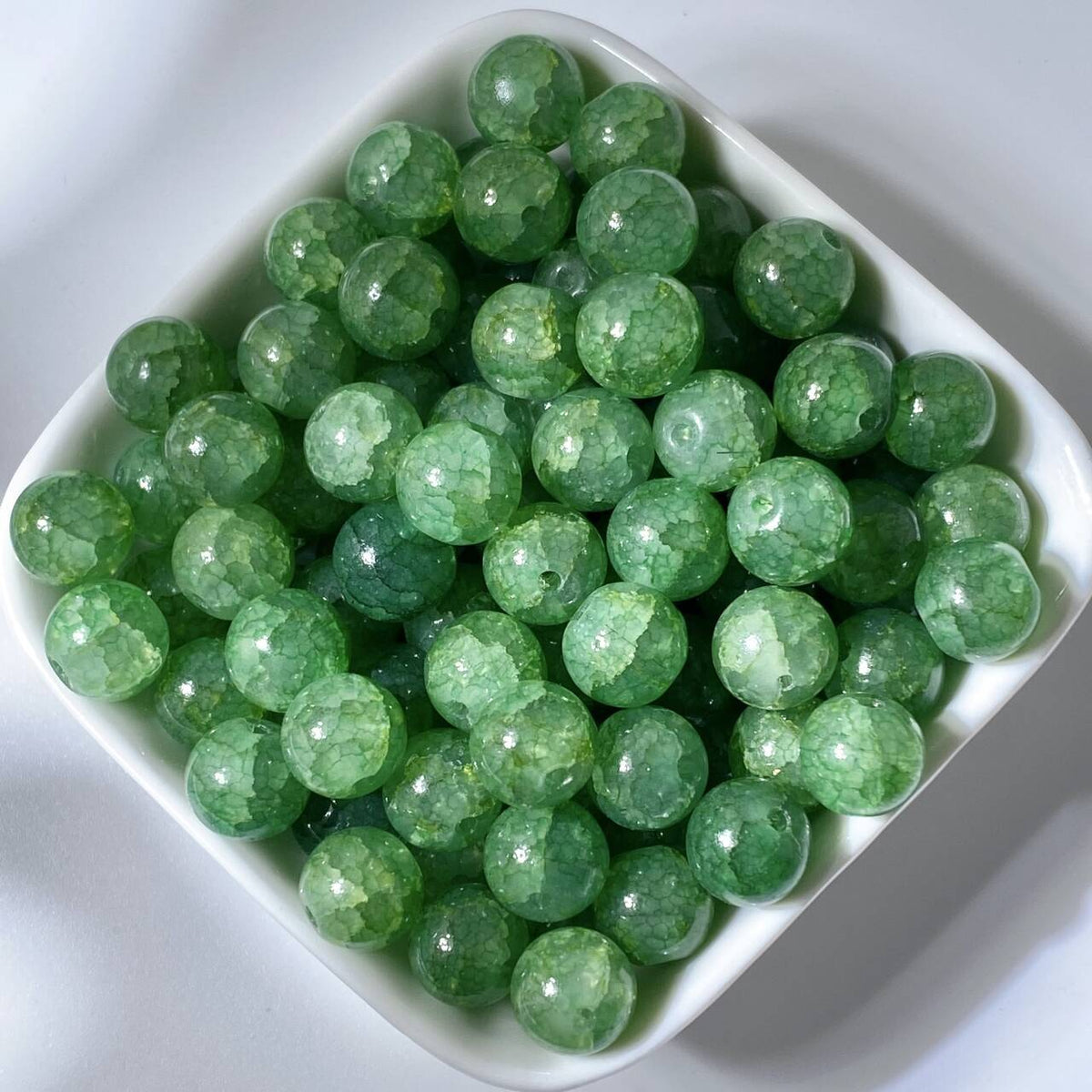 Green 10mm water-dyed jade-style crackle glass beads in a white square dish