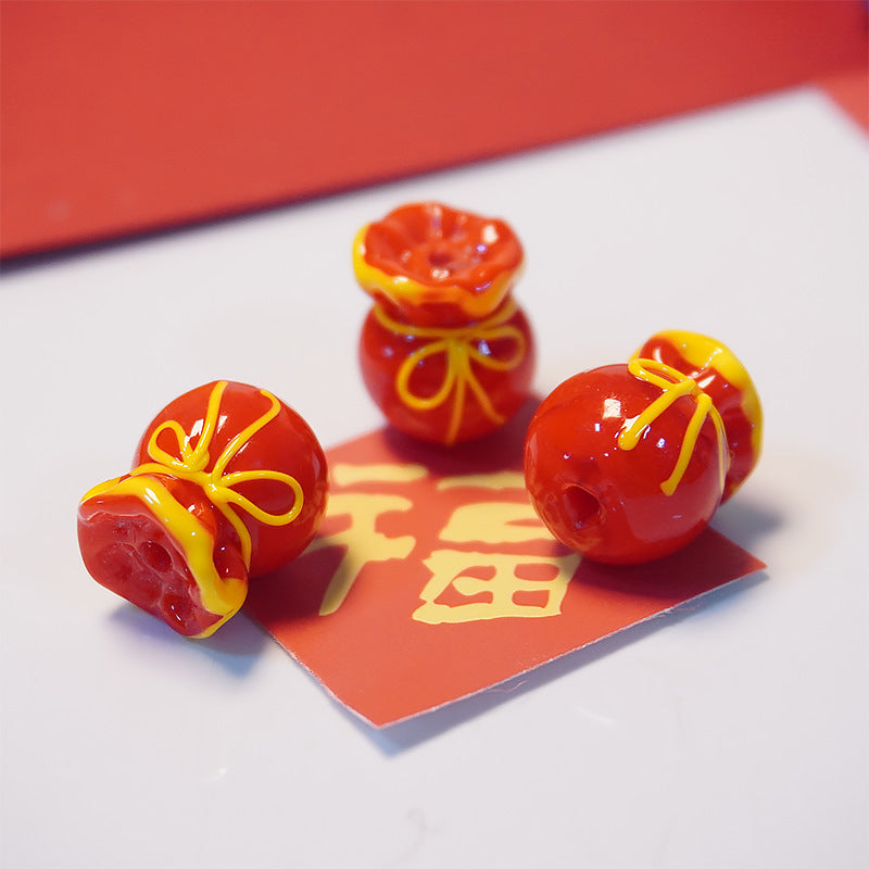 Three glossy red decorative beads shaped like wrapped red envelopes, with yellow trim and bow details, arranged on a red card over a white surface.