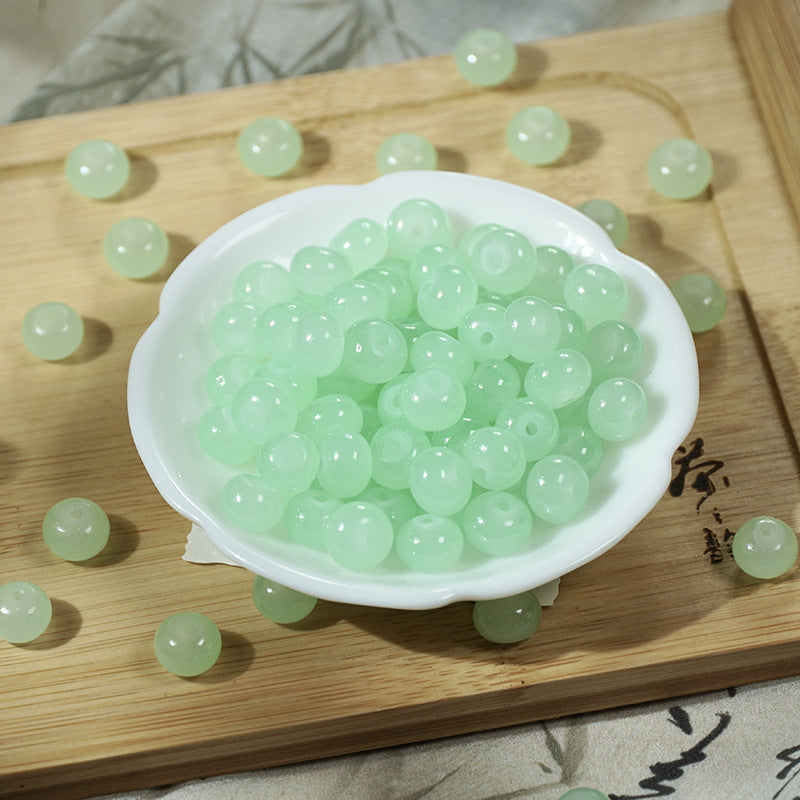 Pale green imitation jade glass beads in a white bowl on a wooden tray