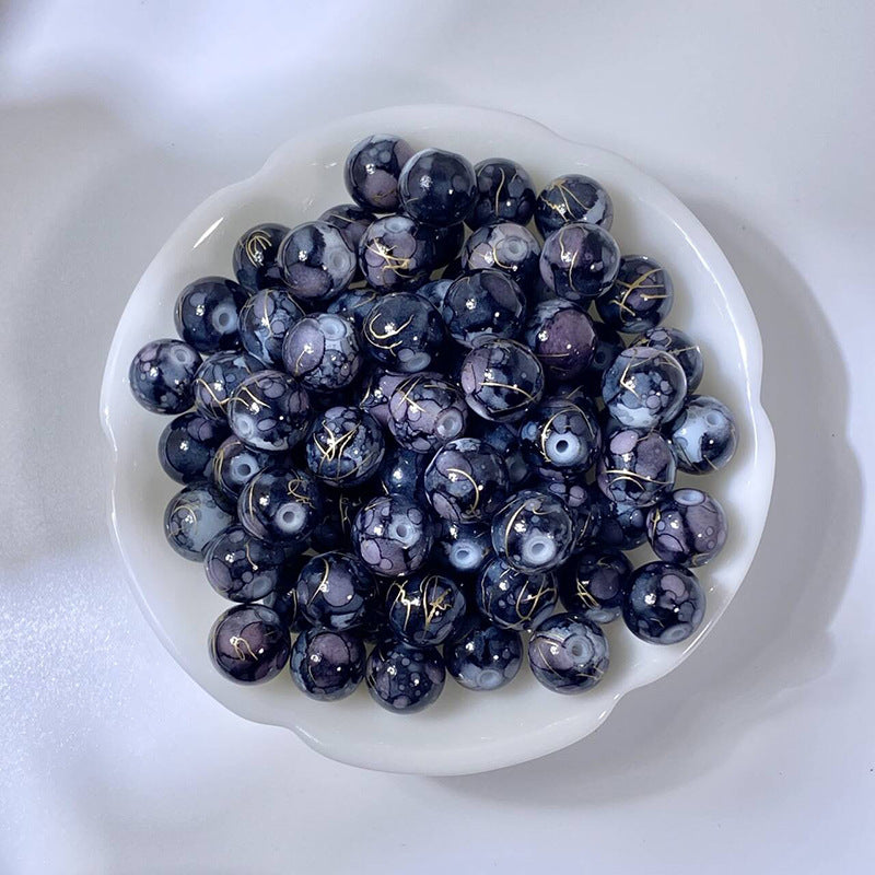 White bowl of marbled black-purple glass beads with gold-silk patterns