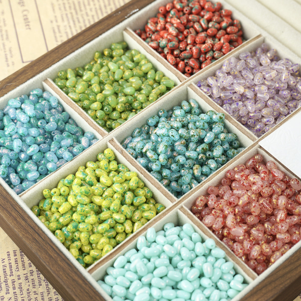 Wooden divided box with colorful speckled glass teardrop beads in turquoise, green, red, pink, and purple