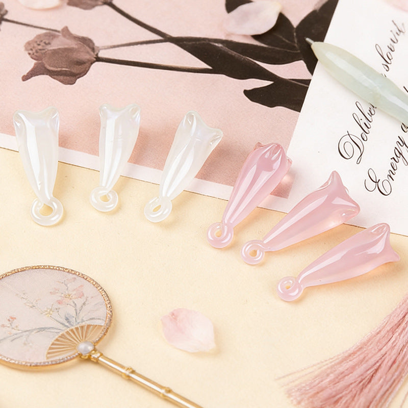 Three white and three pink translucent magnolia flower pendant beads on beige surface with printed card, fan and pink tassel