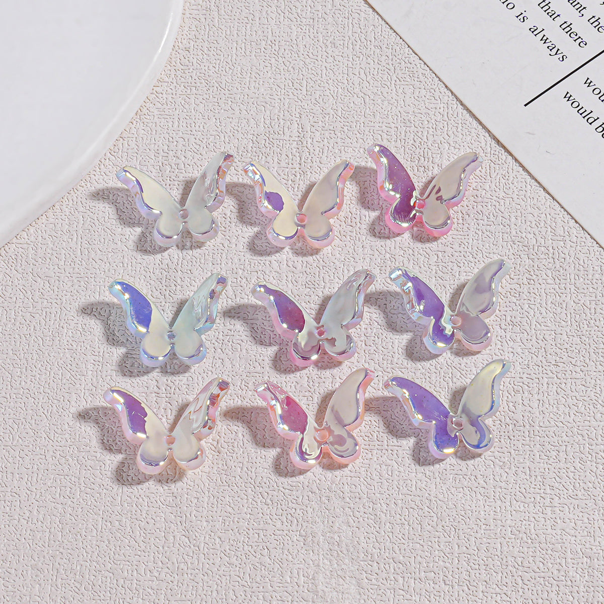 Nine iridescent butterfly acrylic beads in grid showing pastel pink, purple, and blue holographic reflections