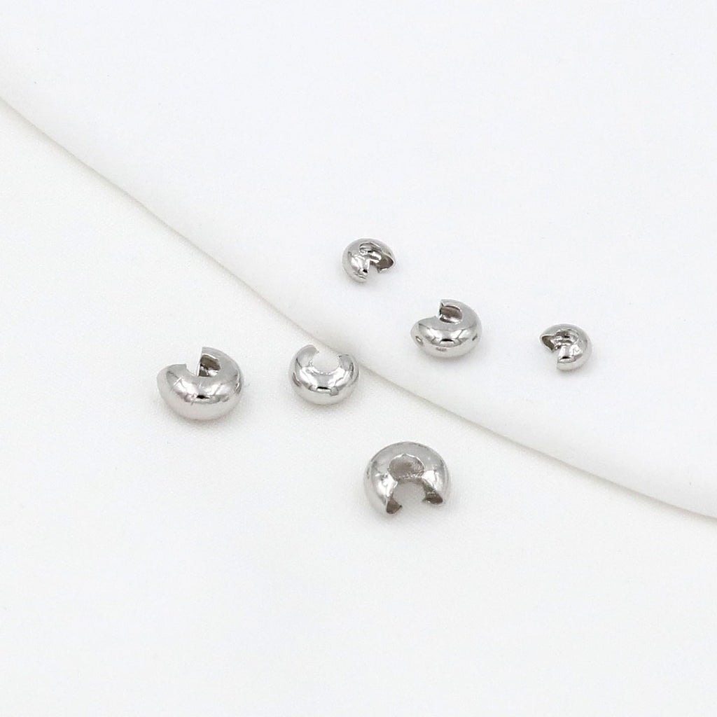 Six small silver C-shaped crimp bead covers scattered on a white background