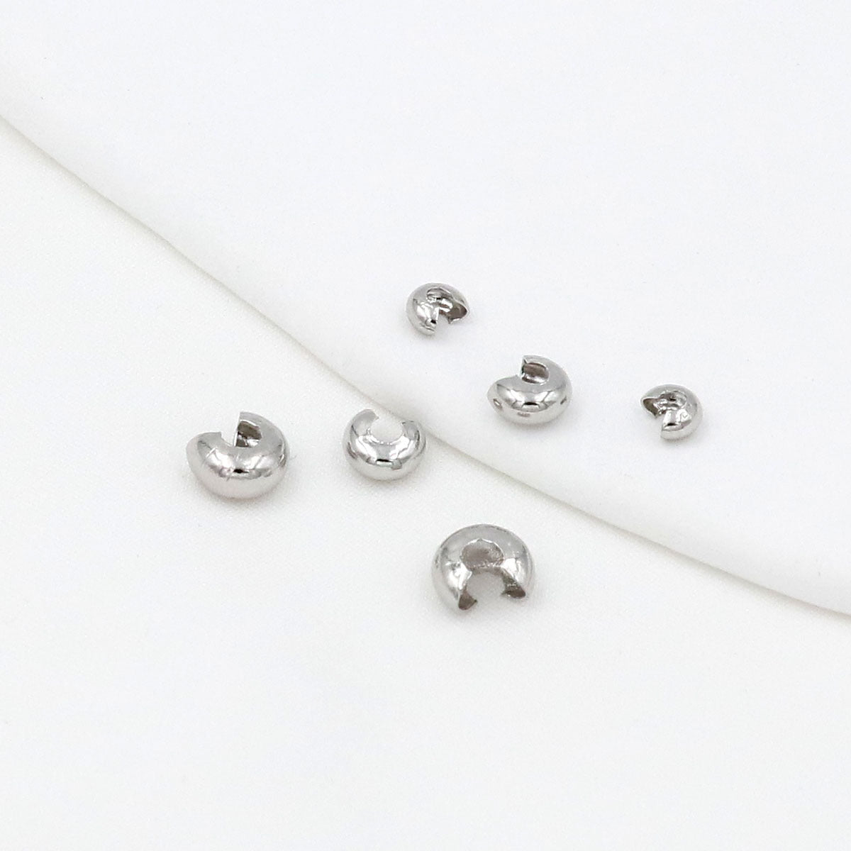 Six small silver C-shaped crimp bead covers scattered on a white background