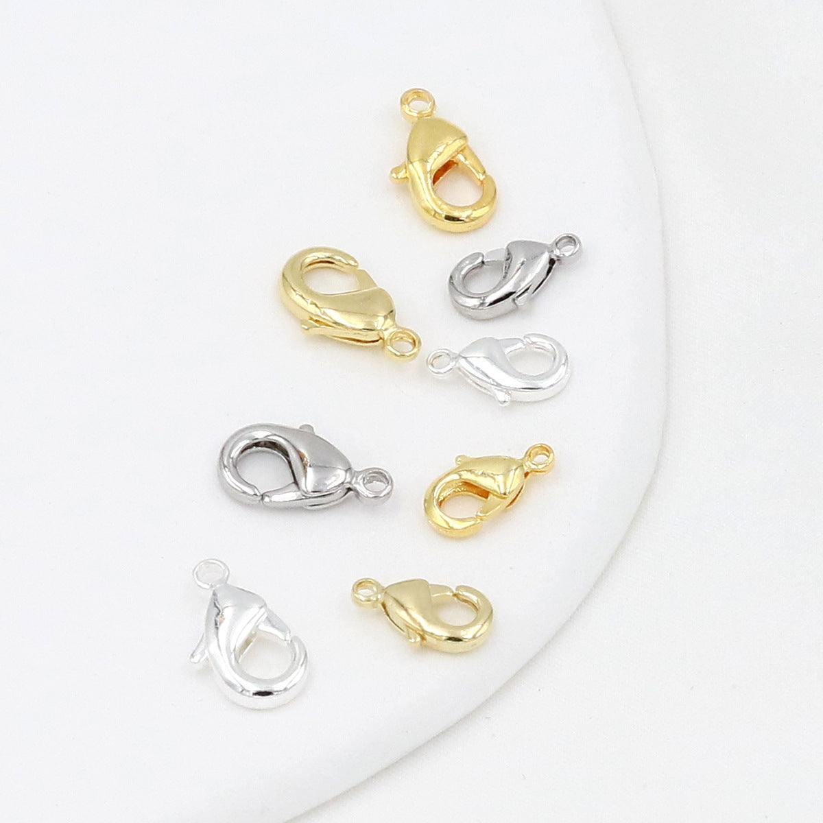 Eight gold and silver teardrop lobster clasps arranged on a white background