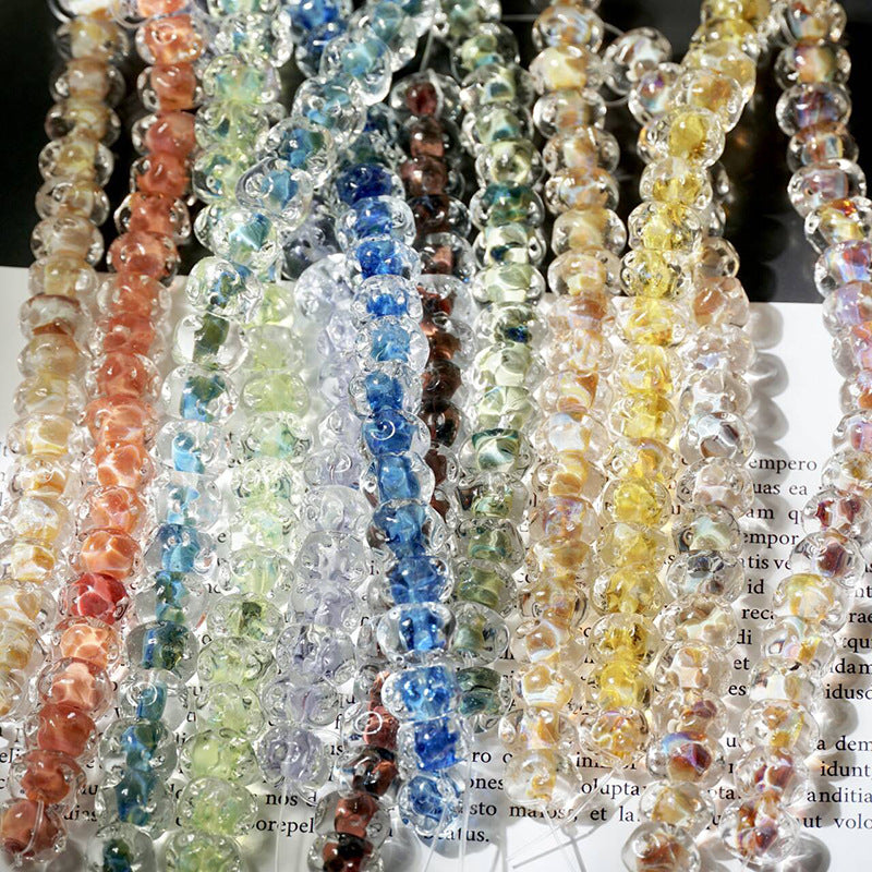 Strands of translucent water-ripple lampwork glass beads in orange, green, blue and yellow hanging vertically in close up