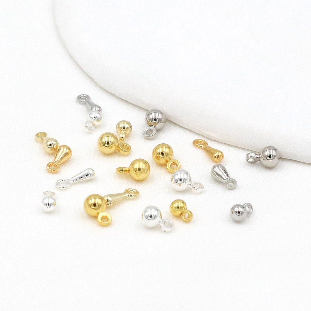 Gold and silver ball and teardrop charms scattered on a white surface with a curved white prop