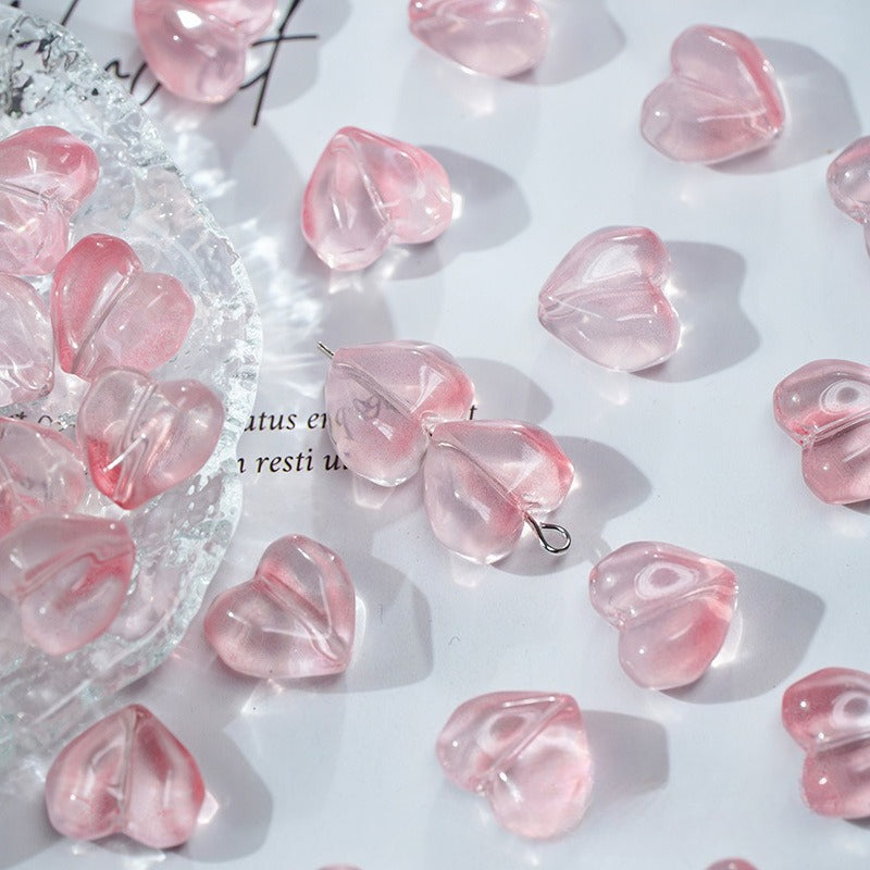 Pink translucent heart-shaped glass beads scattered on a white surface with a clear dish of beads on the left